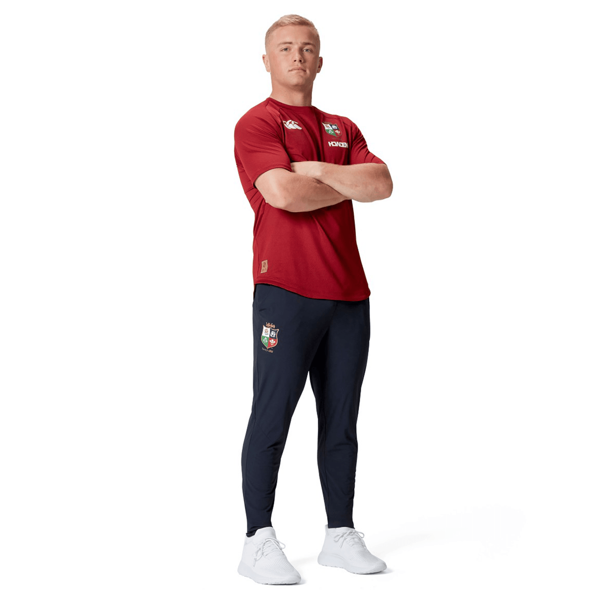 A person in a red shirt and Canterbury British & Irish Lions 2025 Everest Woven Pant stands with arms crossed, looking forward.