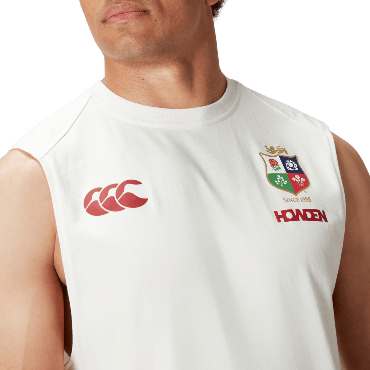 A person is dressed in the British & Irish Lions 25 Cotton Muscle Tank by Canterbury, featuring a sleeveless white design with a crest and logos on the chest, echoing the iconic style of the Canterbury collection.