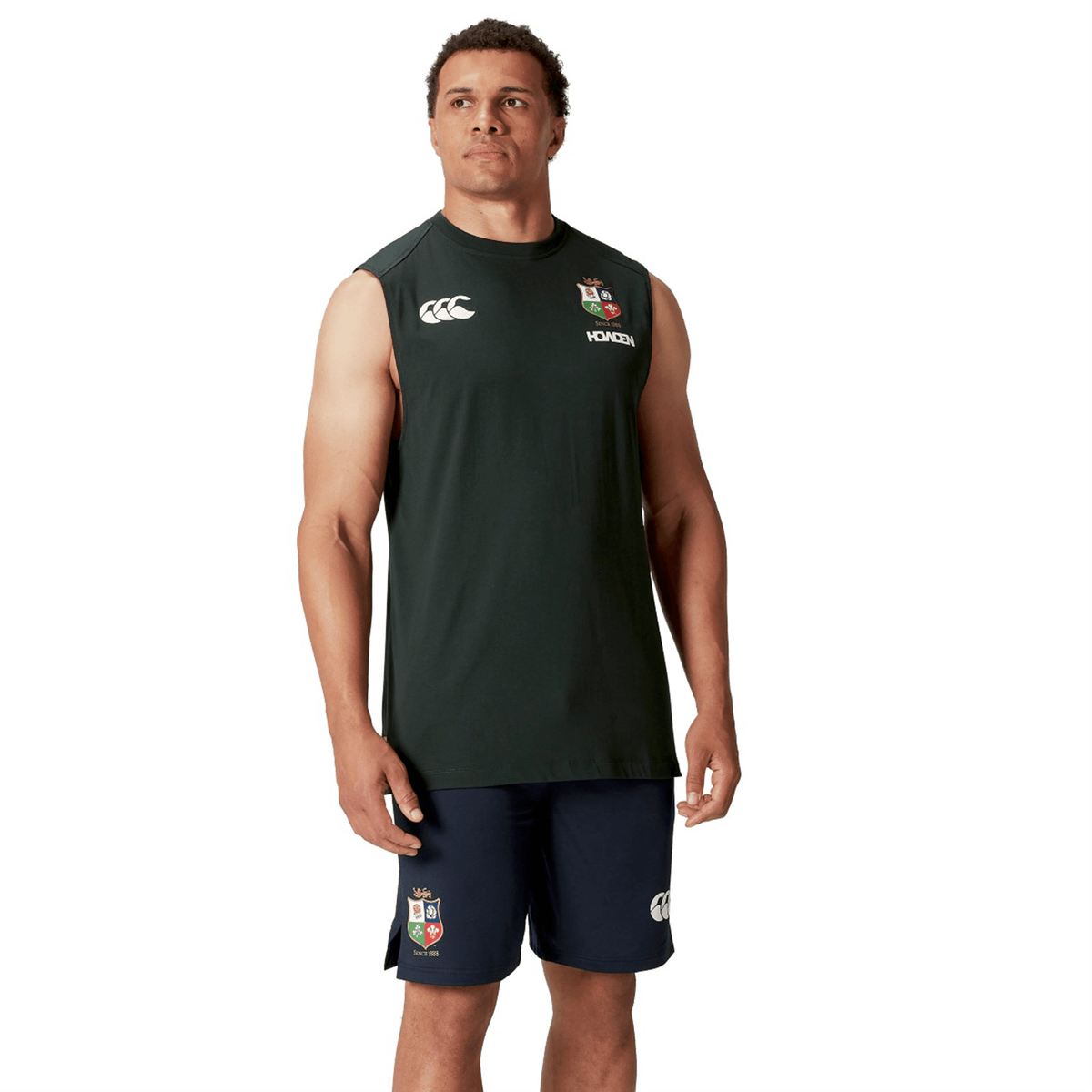 A person wearing the British & Irish Lions 25 Cotton Muscle Tank by Canterbury and matching black shorts, both adorned with logo prints, stands against a white background. The ensemble embodies the sporty elegance synonymous with Canterbury and the British & Irish Lions.