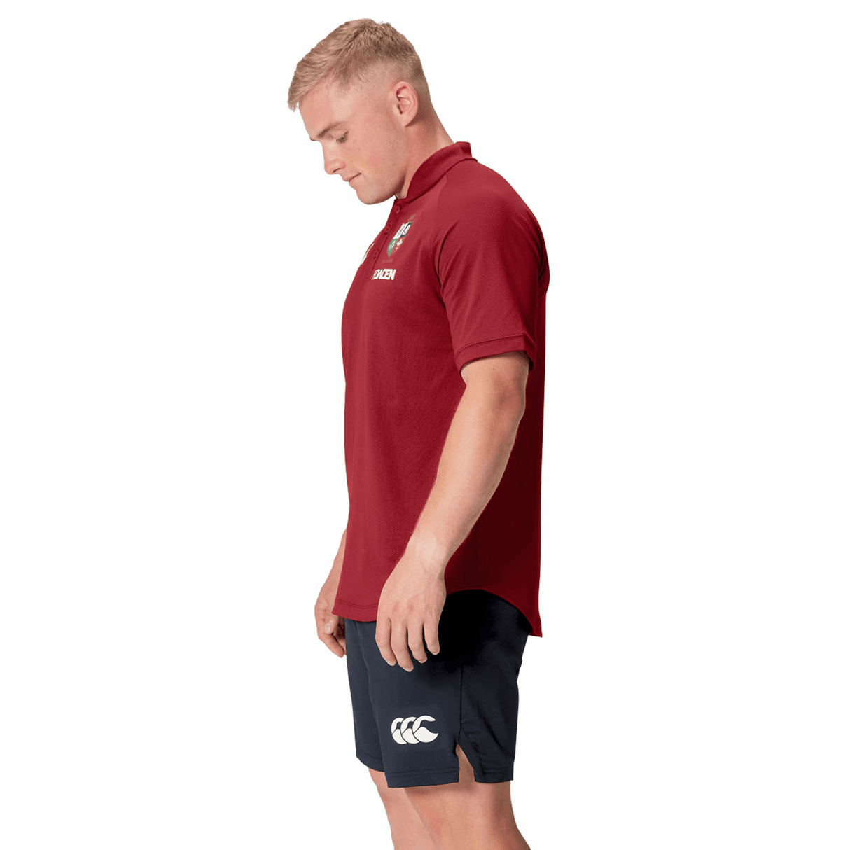 A man wearing the British & Irish Lions 25 Poly Polo by Canterbury, made from breathable fabric, stands against a white background, looking down.