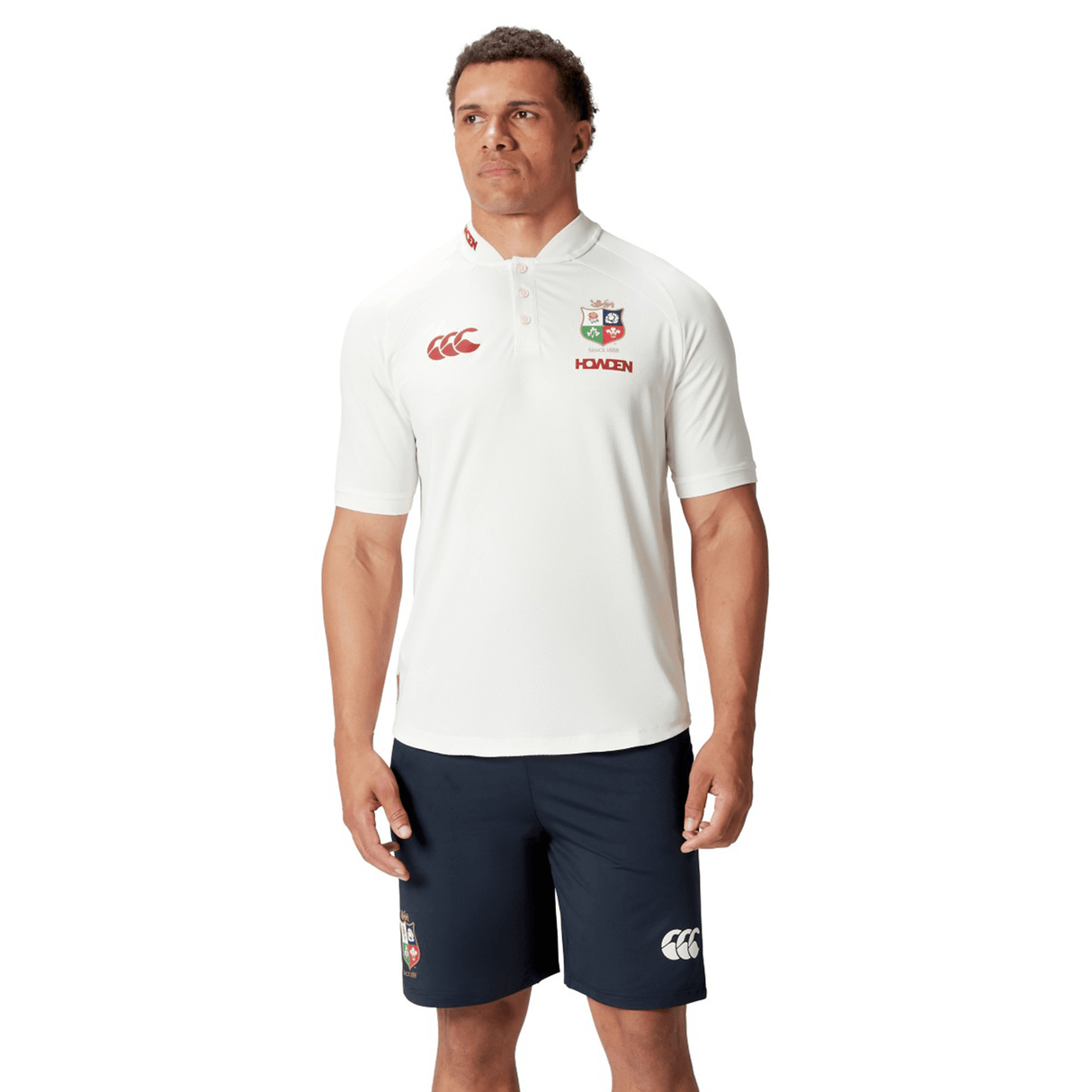 Dressed in a British & Irish Lions 25 Poly Polo by Canterbury and navy shorts, an individual stands against a plain background, capturing the classic style of dedicated Lions fans.