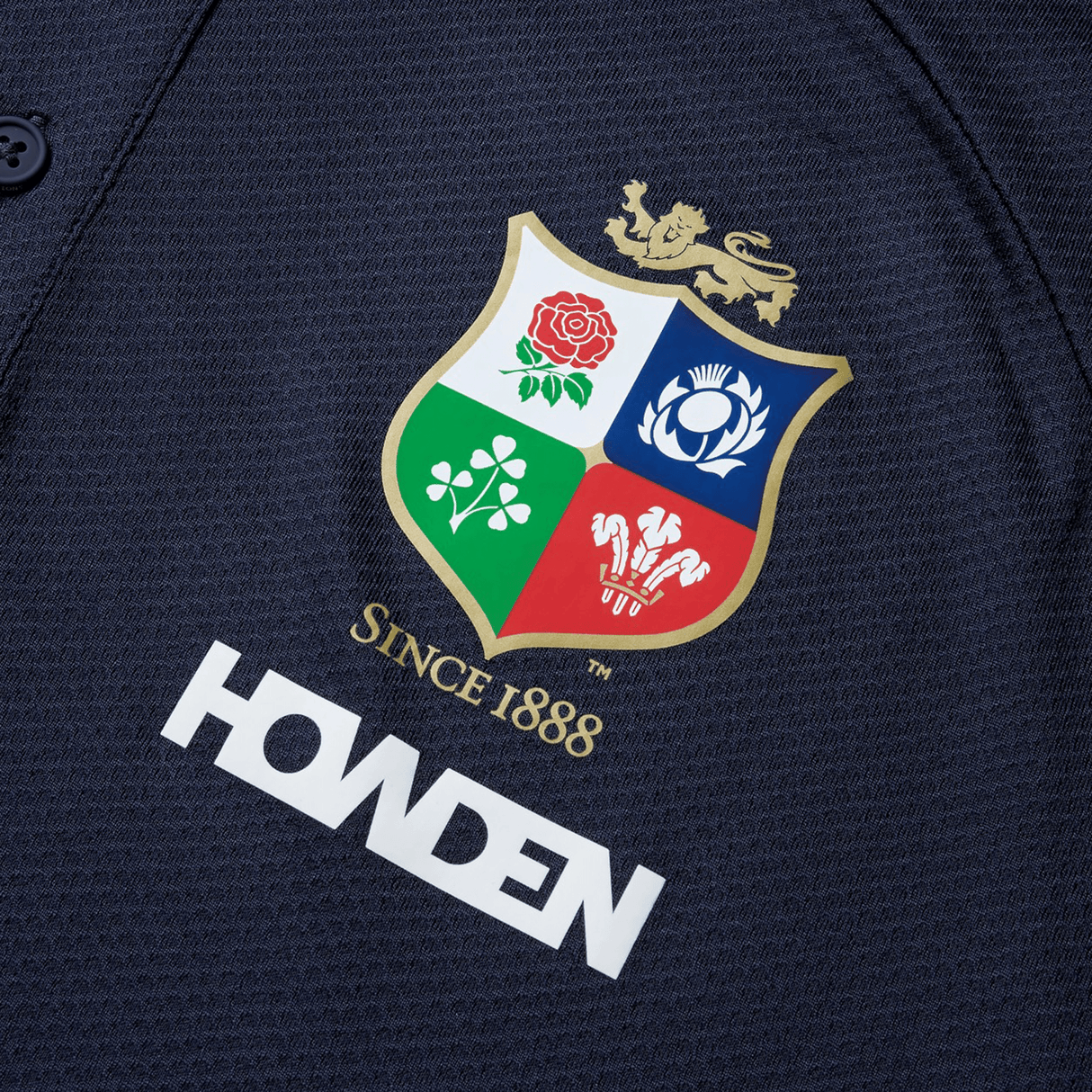 Close-up of a British & Irish Lions 25 Poly Polo by Canterbury, made from quick-drying fabric, showcasing the team's crest and "Howden" sponsor logo on a dark background.