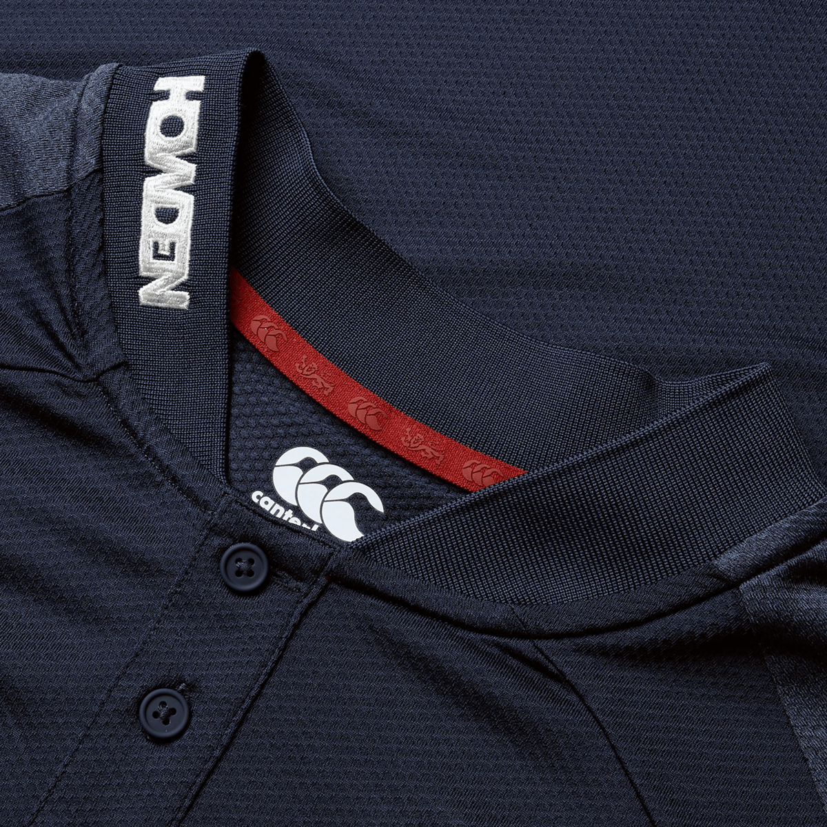 Close-up of the British & Irish Lions 25 Poly Polo by Canterbury, showcasing "HONDEN" on the collar and Canterbury logo, crafted from quick-drying, breathable fabric. The design is inspired by a dark rugby jersey and features red inner neck detailing.
