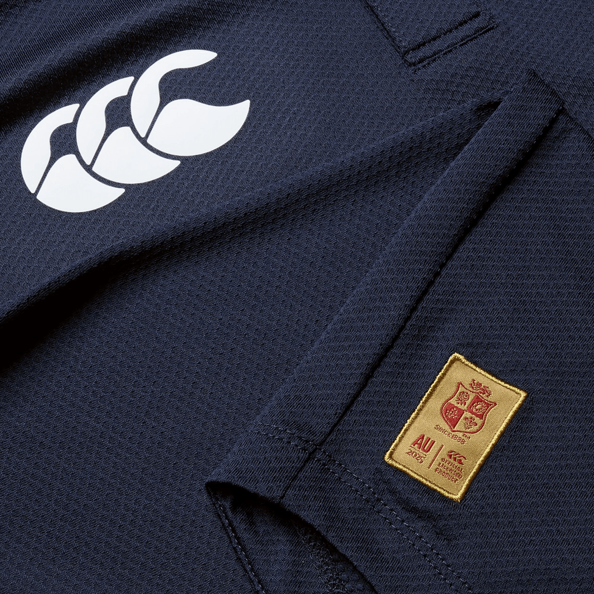 Close-up of the British & Irish Lions 25 Poly Polo by Canterbury in navy blue, crafted from quick-drying fabric, showcasing a white logo on the right shoulder and an embroidered "AU" crest on the left side.