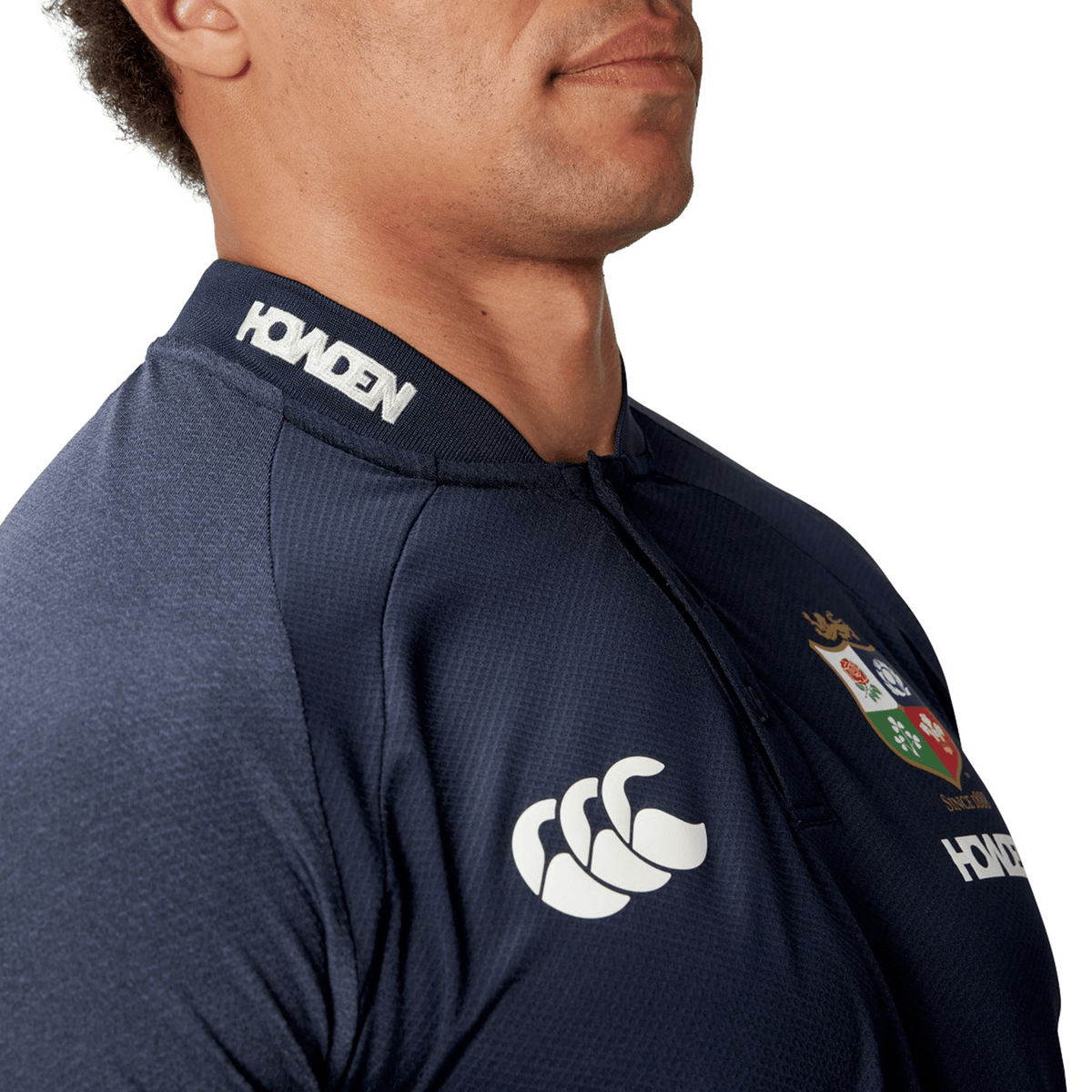 A person wearing the British & Irish Lions 25 Poly Polo by Canterbury, a navy sports jersey featuring white logos on the chest and collar, crafted from quick-drying, breathable fabric.