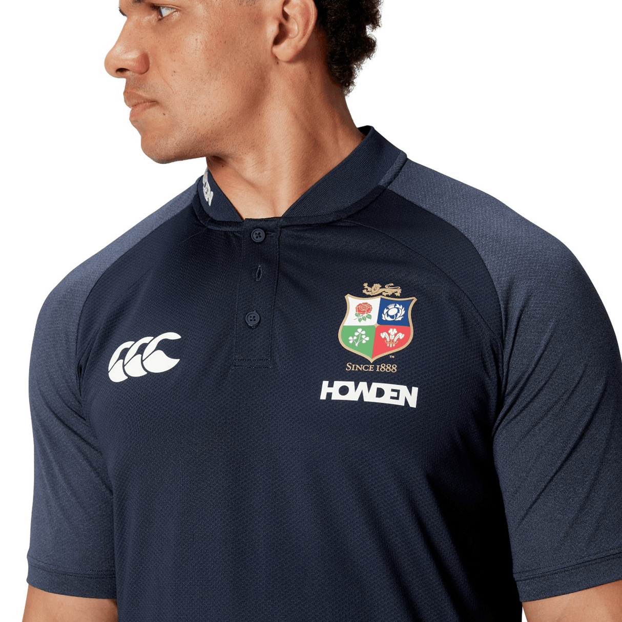 A person wearing a dark blue Canterbury British & Irish Lions 25 Poly Polo, featuring logos and made from quick-drying fabric, glances to the side.