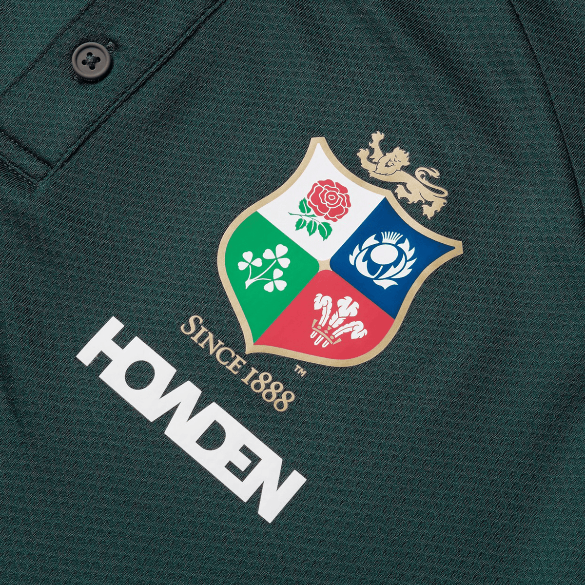 Close-up of the British & Irish Lions 25 Poly Polo by Canterbury in dark green, made from breathable fabric, showcasing a multi-colored crest with a lion and various emblems above the words "Since 1888" and the Howden logo.