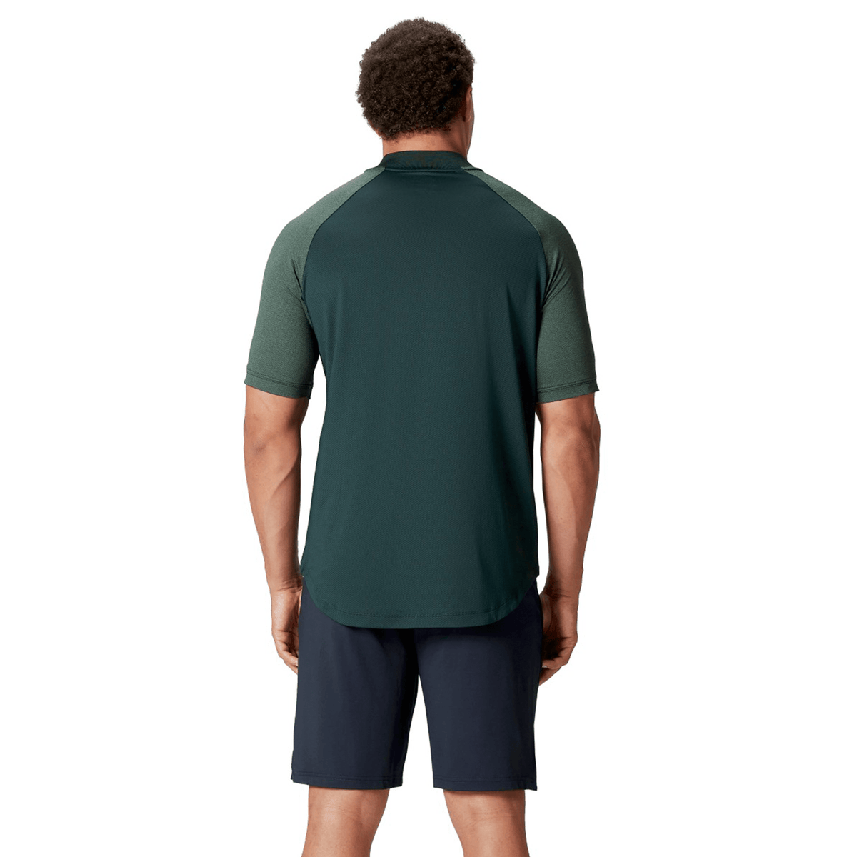 A person stands with their back turned, wearing a dark green British & Irish Lions 25 Poly Polo from Canterbury, crafted from quick-drying fabric, paired with dark shorts, set against a plain white background.