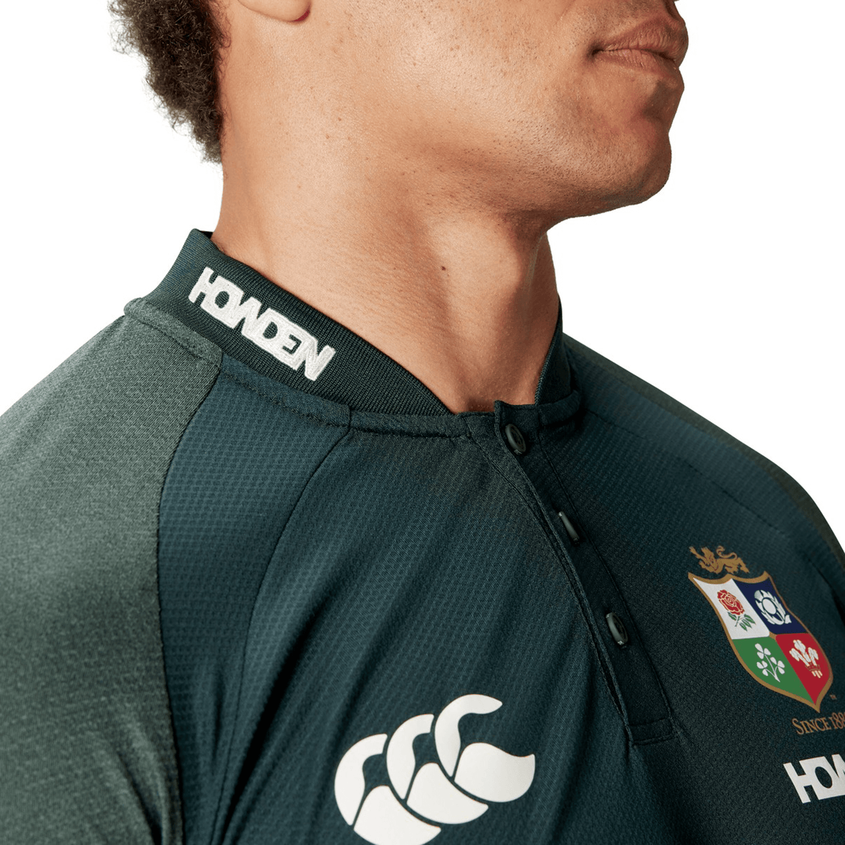 A person wearing a British & Irish Lions 25 Poly Polo crafted by Canterbury, featuring a dark green color, iconic emblems, and "HONDEN" on the collar, made with quick-drying fabric perfect for any match day.