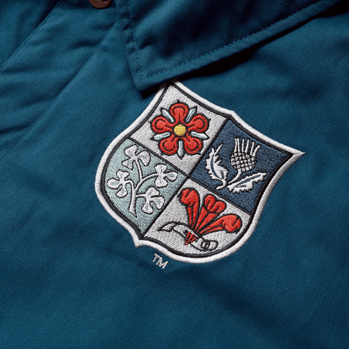 A close-up of the British & Irish Lions 2025 Heritage Quilted Jacket by Canterbury in blue, featuring an embroidered shield logo with a red rose, thistle, shamrock, and daffodil—symbolic emblems of the British & Irish Lions.