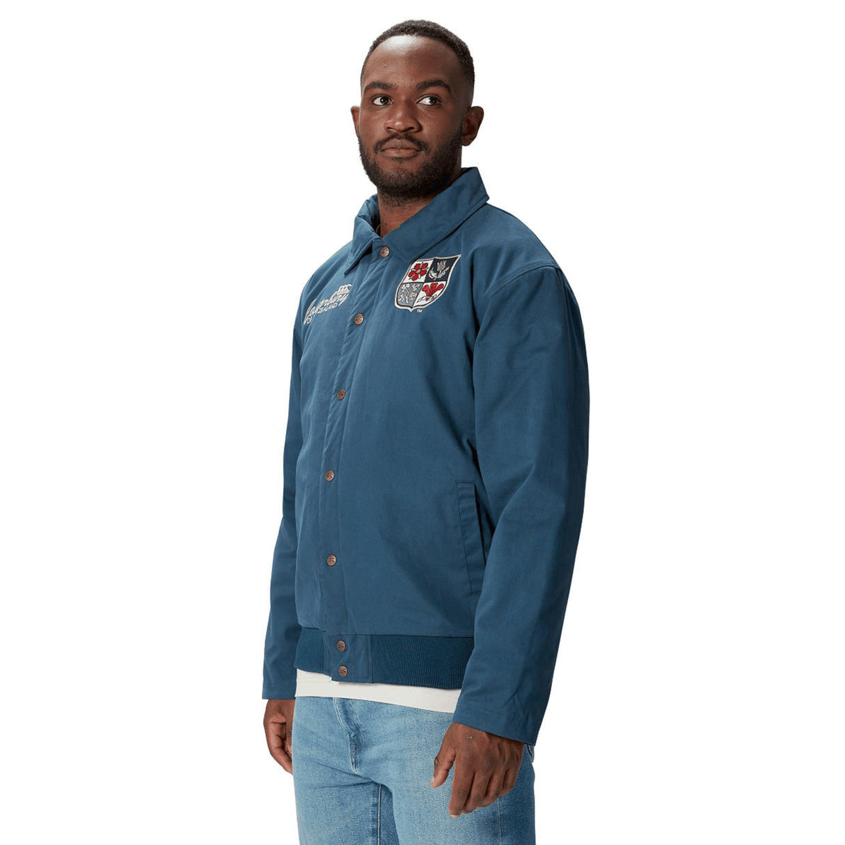 A man sporting the British & Irish Lions 2025 Heritage Quilted Jacket by Canterbury in blue, featuring badges on the chest, combined stylishly with light blue jeans, radiates classic Canterbury charm.