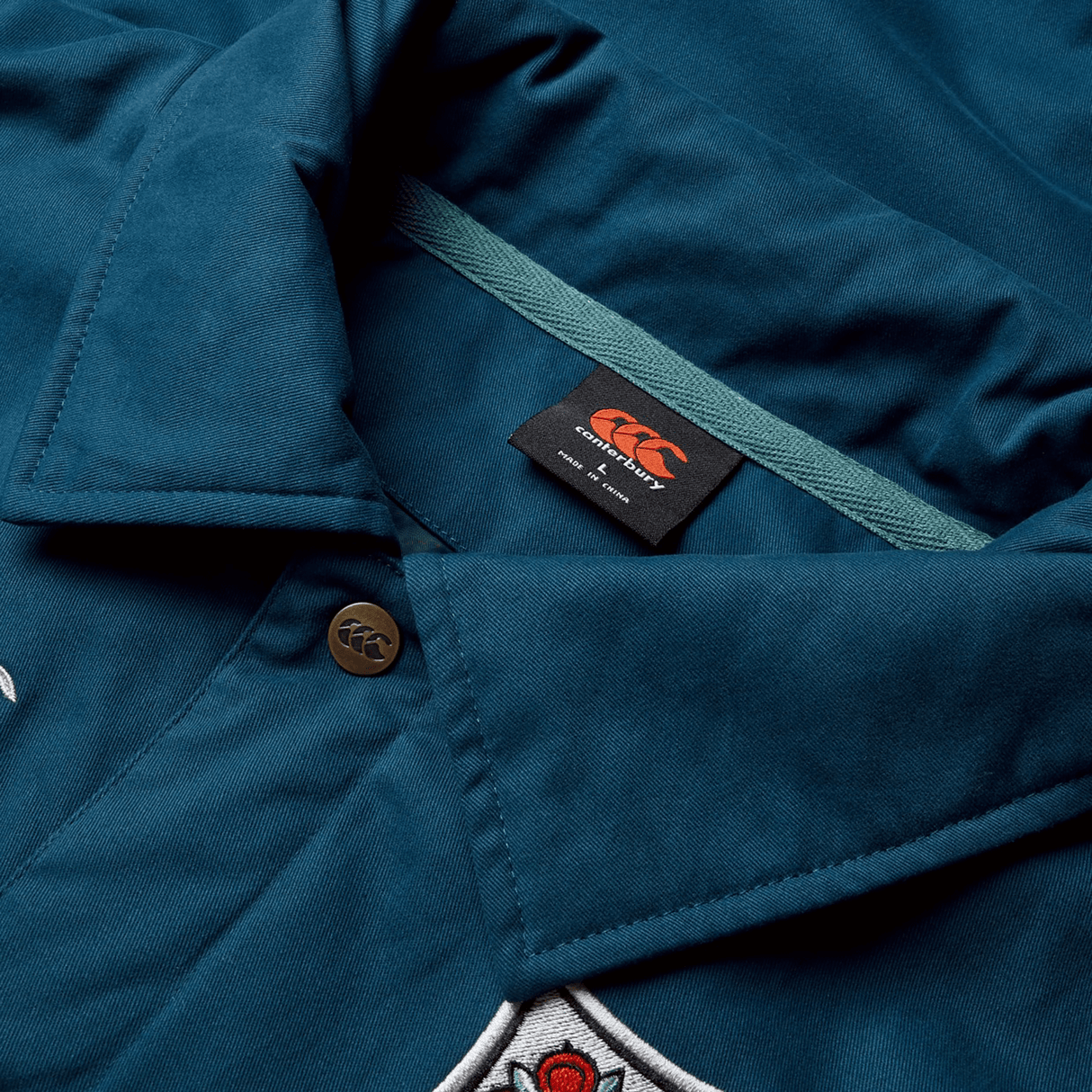 Close-up of the collar of a Canterbury British & Irish Lions 2025 Heritage Quilted Jacket, detailed with a button, tag, and part of an embroidered design that reflects the classic style associated with British & Irish Lions attire.