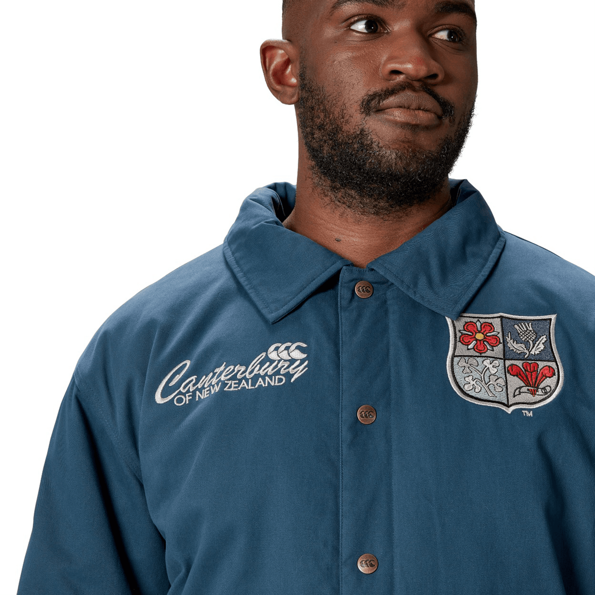 A man wears the British & Irish Lions 2025 Heritage Quilted Jacket by Canterbury, showcasing a crest and embroidered logo in a blue design that evokes the classic style linked with the esteemed British & Irish Lions.
