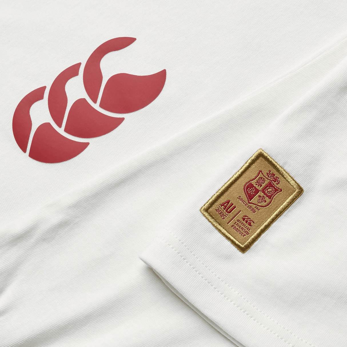 The Women's British & Irish Lions 25 Cotton Jersey Tee by Canterbury, made from organic cotton, showcases a red triple-leaf logo on the left and an embroidered golden shield patch on the right bearing a coat of arms and the letters "AU".