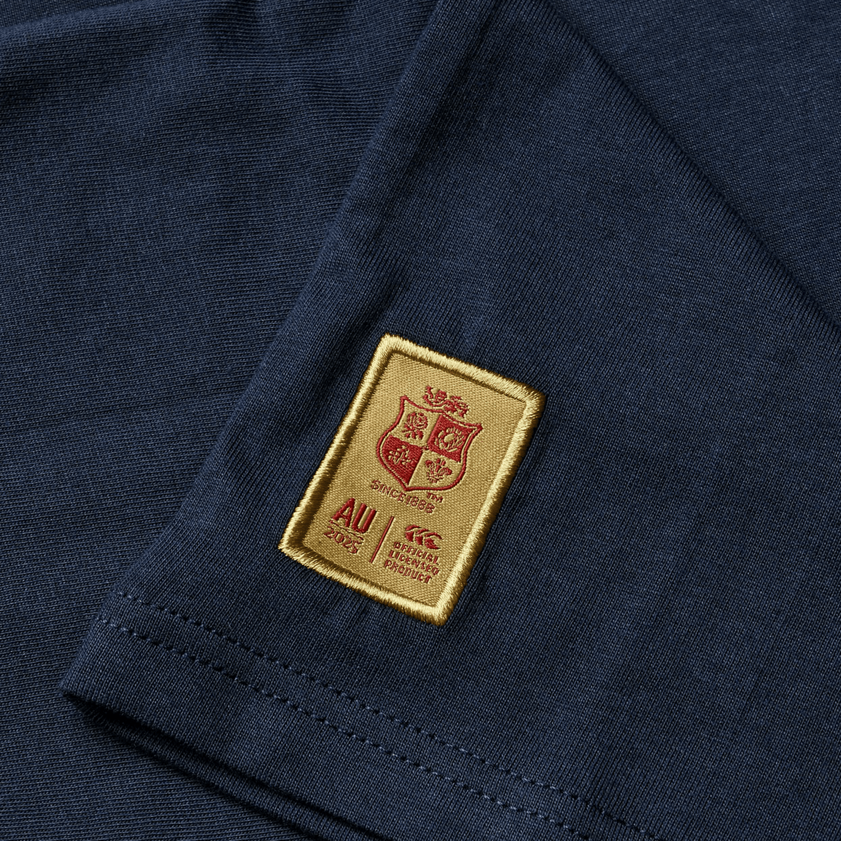 A dark youth cotton jersey tee by Canterbury featuring a gold and red patch with the "AU 2025" crest and "official product" text—perfect for any British & Irish Lions supporter.
