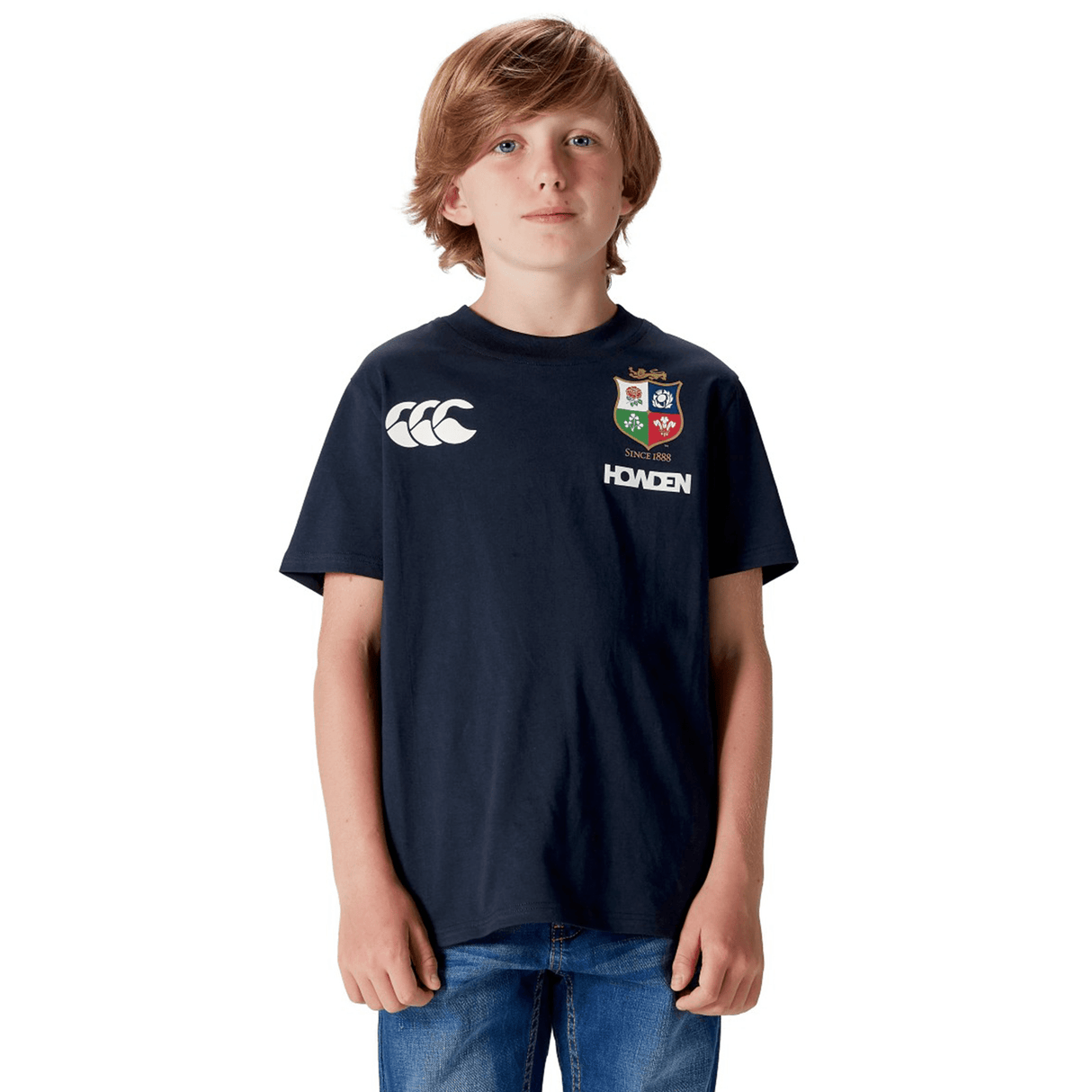 A boy in a Canterbury Youth British & Irish Lions 2025 Cotton Jersey Tee and blue jeans, against a white background, exudes true rugby supporter spirit.