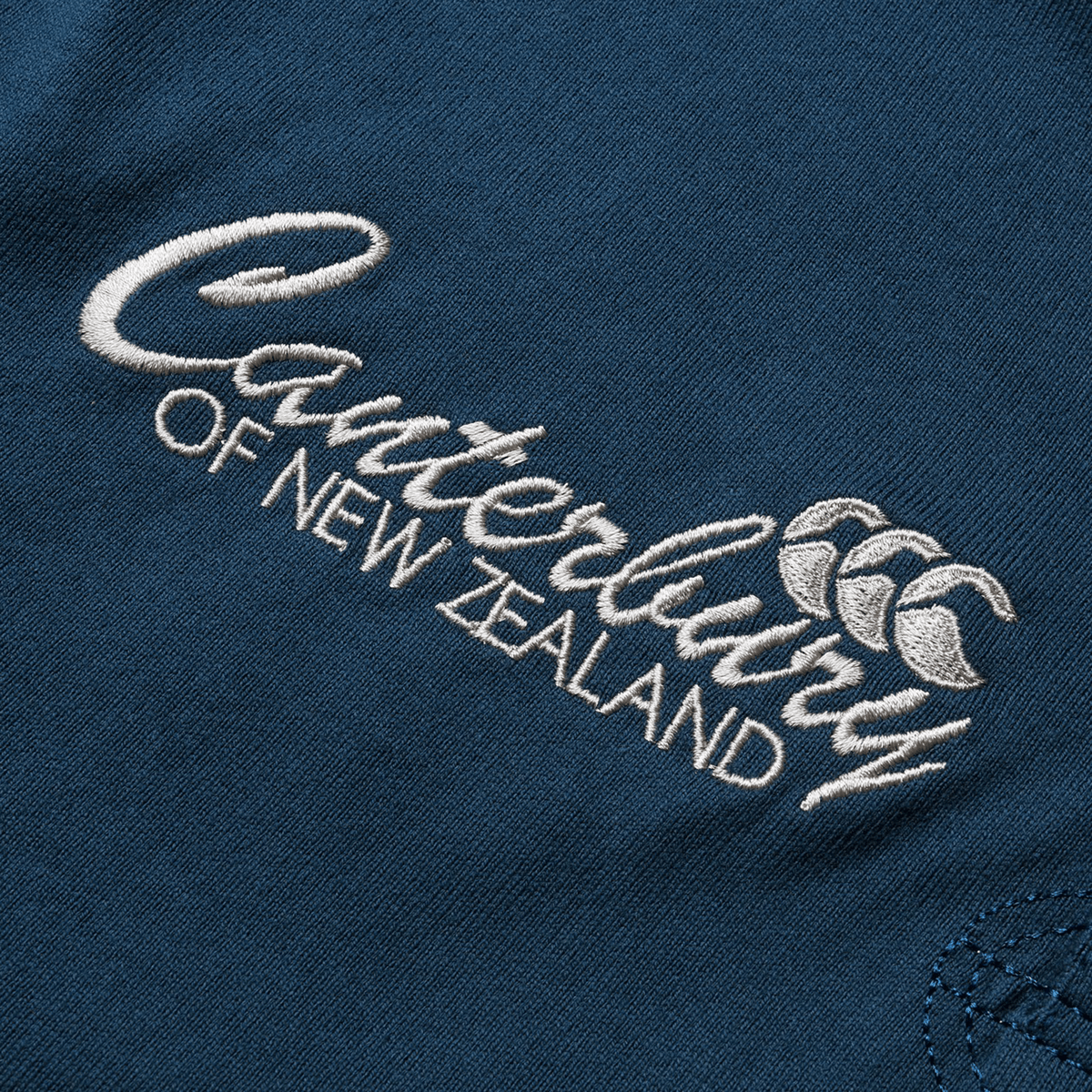 A stitched emblem of "Canterbury" adorns the blue fabric, showcasing the iconic Canterbury symbol and encapsulating the spirit of a British & Irish Lions 2025 Heritage Jersey by Canterbury.