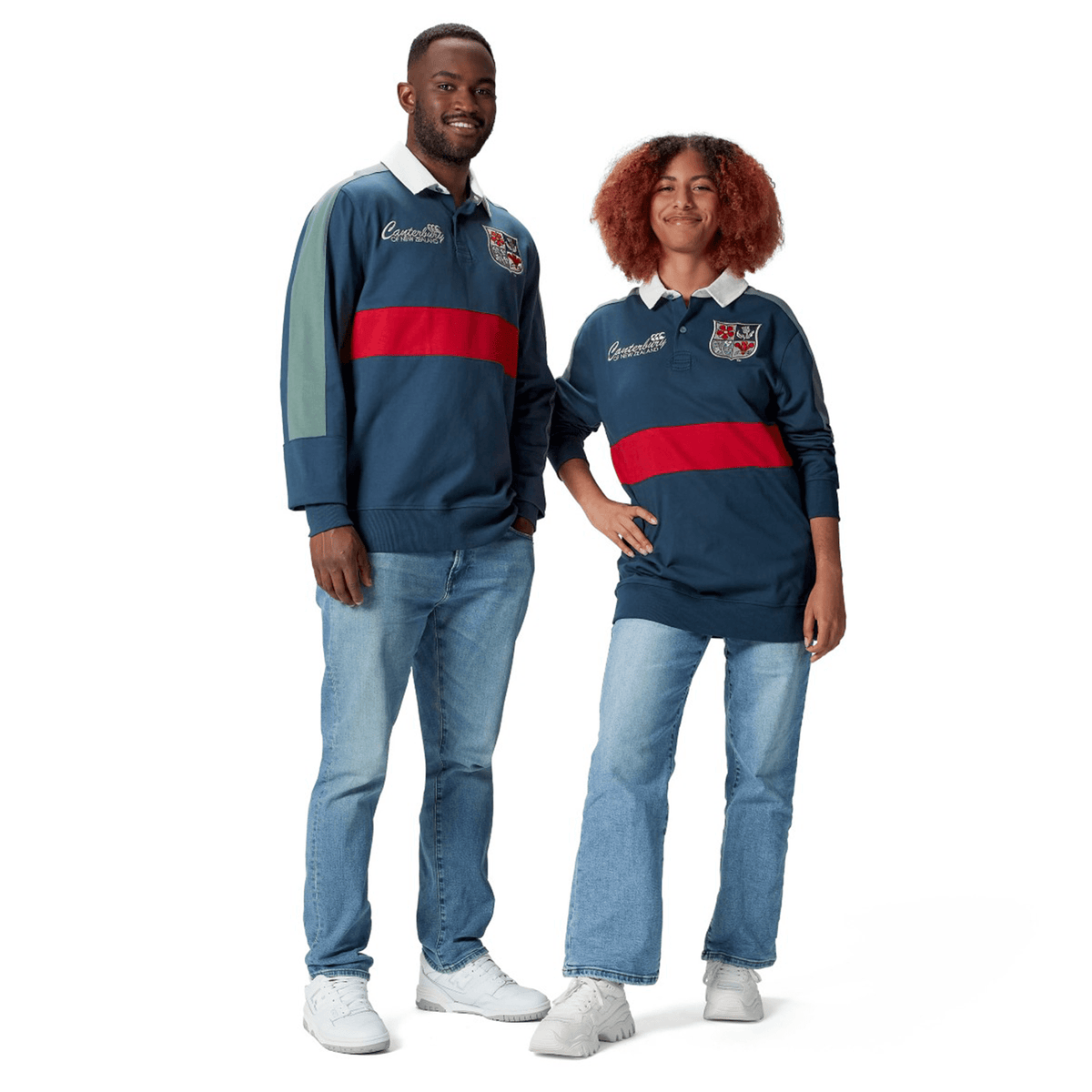A man and woman wearing matching blue and red British & Irish Lions 2025 Heritage Jerseys by Canterbury with jeans stand side by side, smiling.