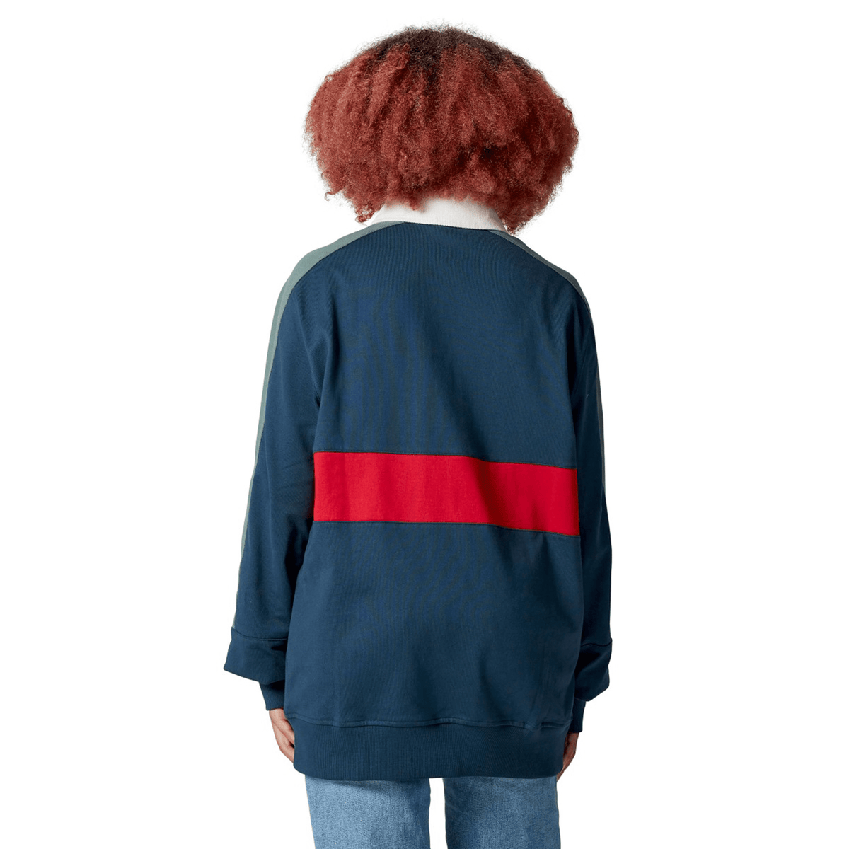 A person with curly hair, wearing the classic navy British & Irish Lions 2025 Heritage Jersey by Canterbury featuring a red stripe across the back, stands facing away.