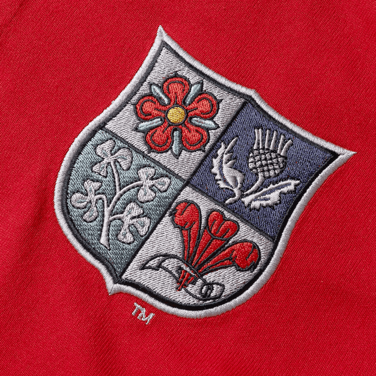 The British & Irish Lions 2025 Heritage Jersey by Canterbury features an embroidered crest on red fabric, divided into four sections showcasing a rose, shamrocks, a thistle, and daffodils—symbols of its proud tradition.