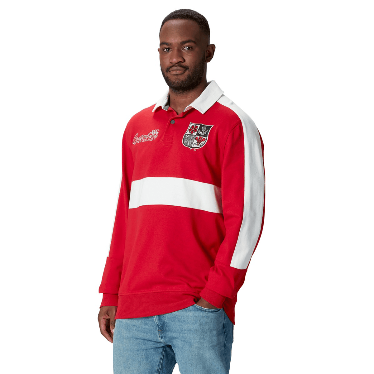 A man wearing a British & Irish Lions 2025 Heritage Jersey by Canterbury, featuring white stripes, pairs it with jeans as he stands against a white background.