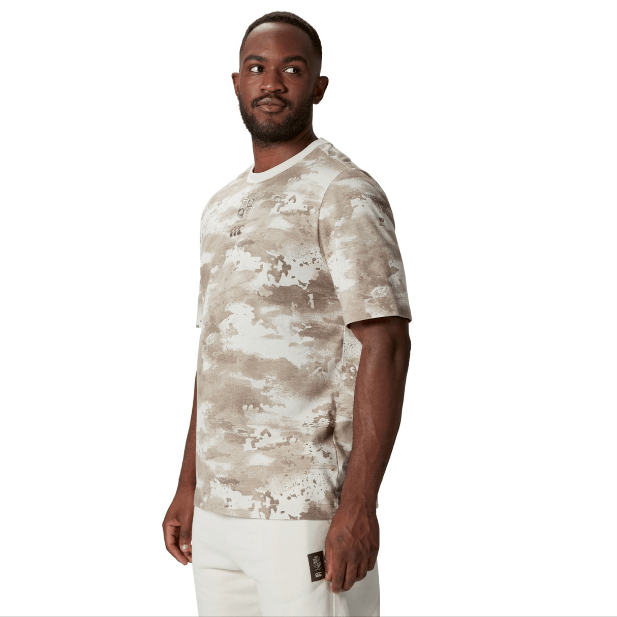 A person wearing a British & Irish Lions 2025 Camo Tee by Canterbury paired with light-colored pants stands against a plain white background, exuding a subtle yet adventurous vibe.