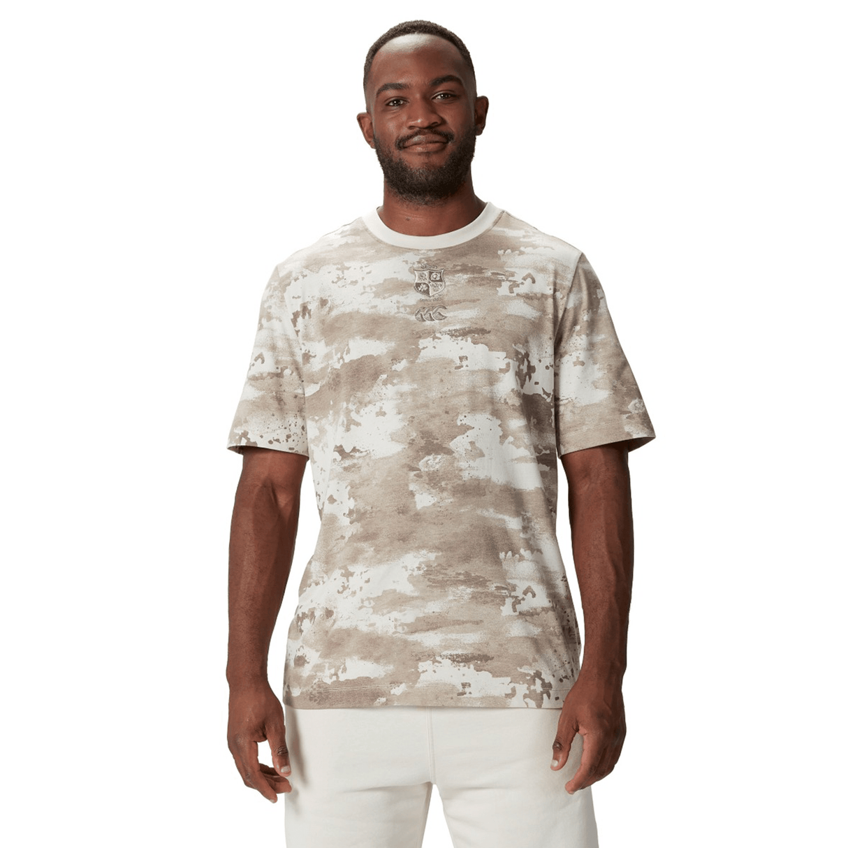 A man wears the British & Irish Lions 2025 Camo Tee by Canterbury, styled with crisp white pants, standing against a pristine white background.