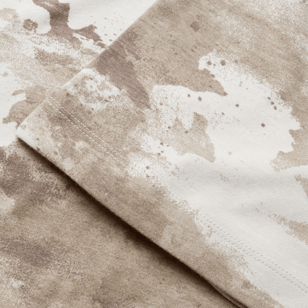 Close-up of fabric with a beige and white abstract pattern, reminiscent of the British & Irish Lions 2025 Camo Tee by Canterbury, showing the edge of a seam.