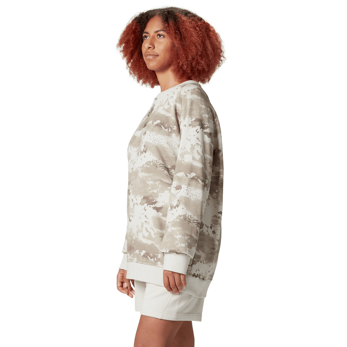 A person with curly hair confidently poses against a white background, modeling the British & Irish Lions 25 Camo Crew Sweatshirt by Canterbury paired with light shorts.