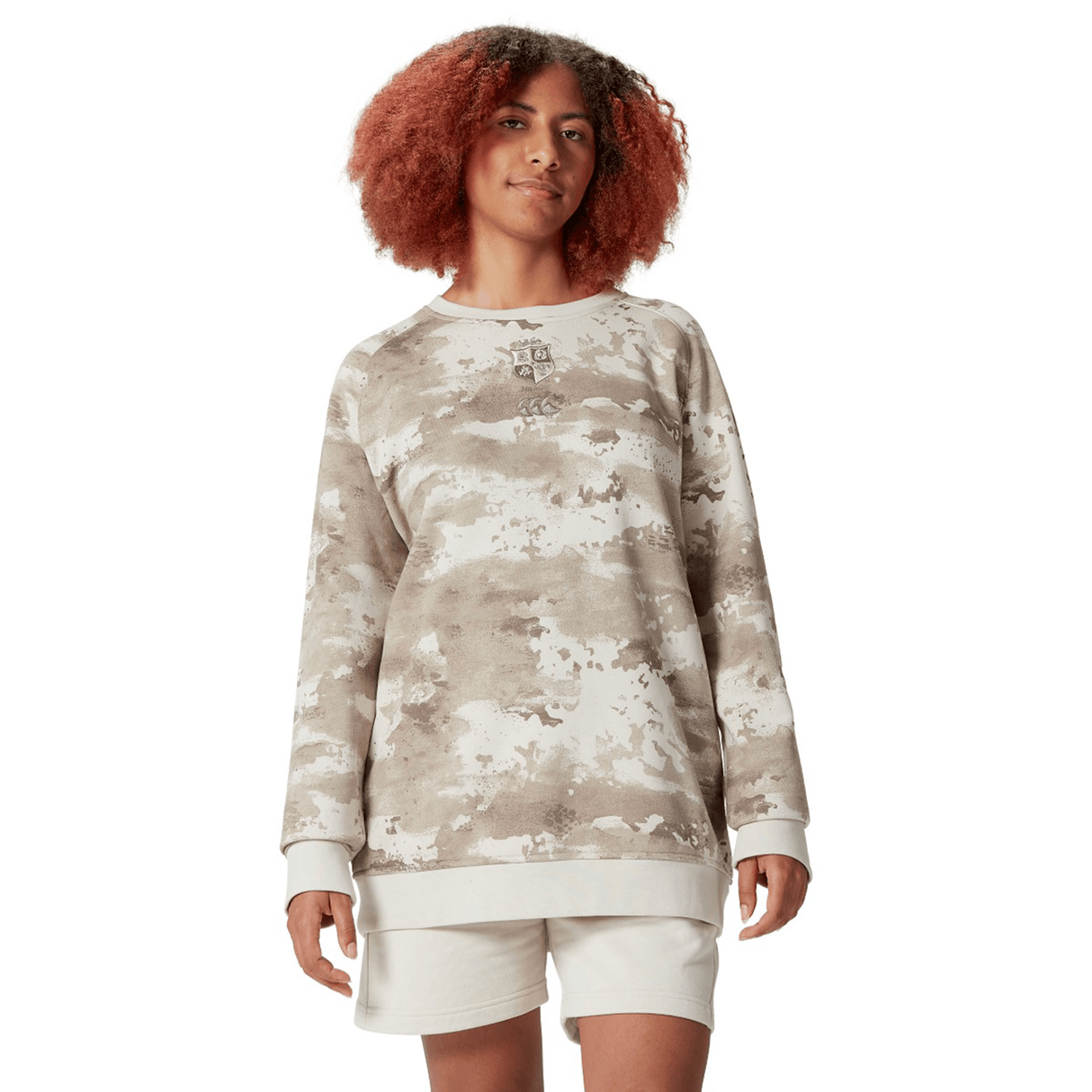 A person dressed in a beige British & Irish Lions 25 Camo Crew Sweatshirt by Canterbury and shorts stands against a plain white background, subtly showcasing the style reminiscent of the brand.