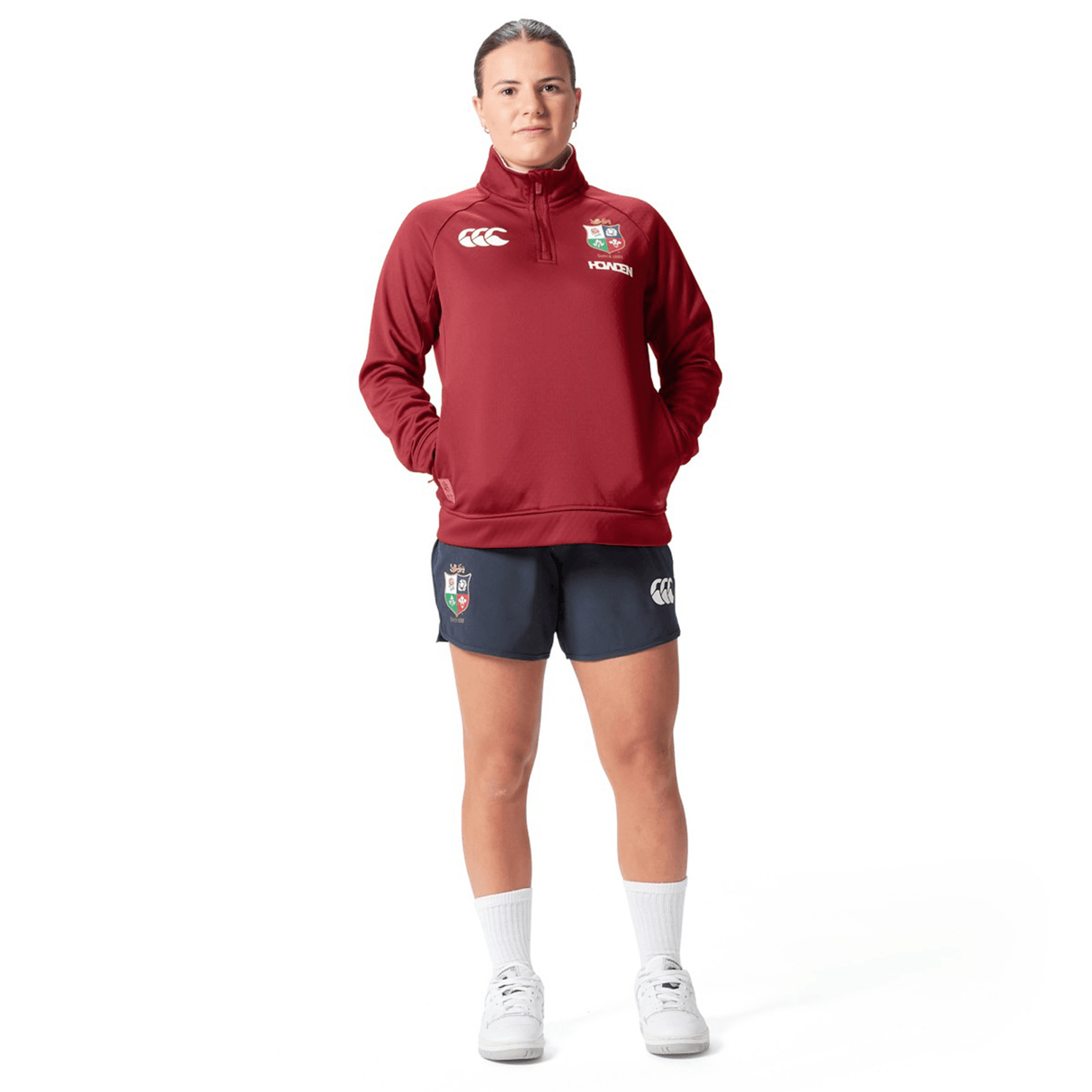 Clad in the Women's British & Irish Lions 2025 1/4 Zip Fleece by Canterbury, with its striking red and navy hues, a person exudes confidence against a white backdrop.