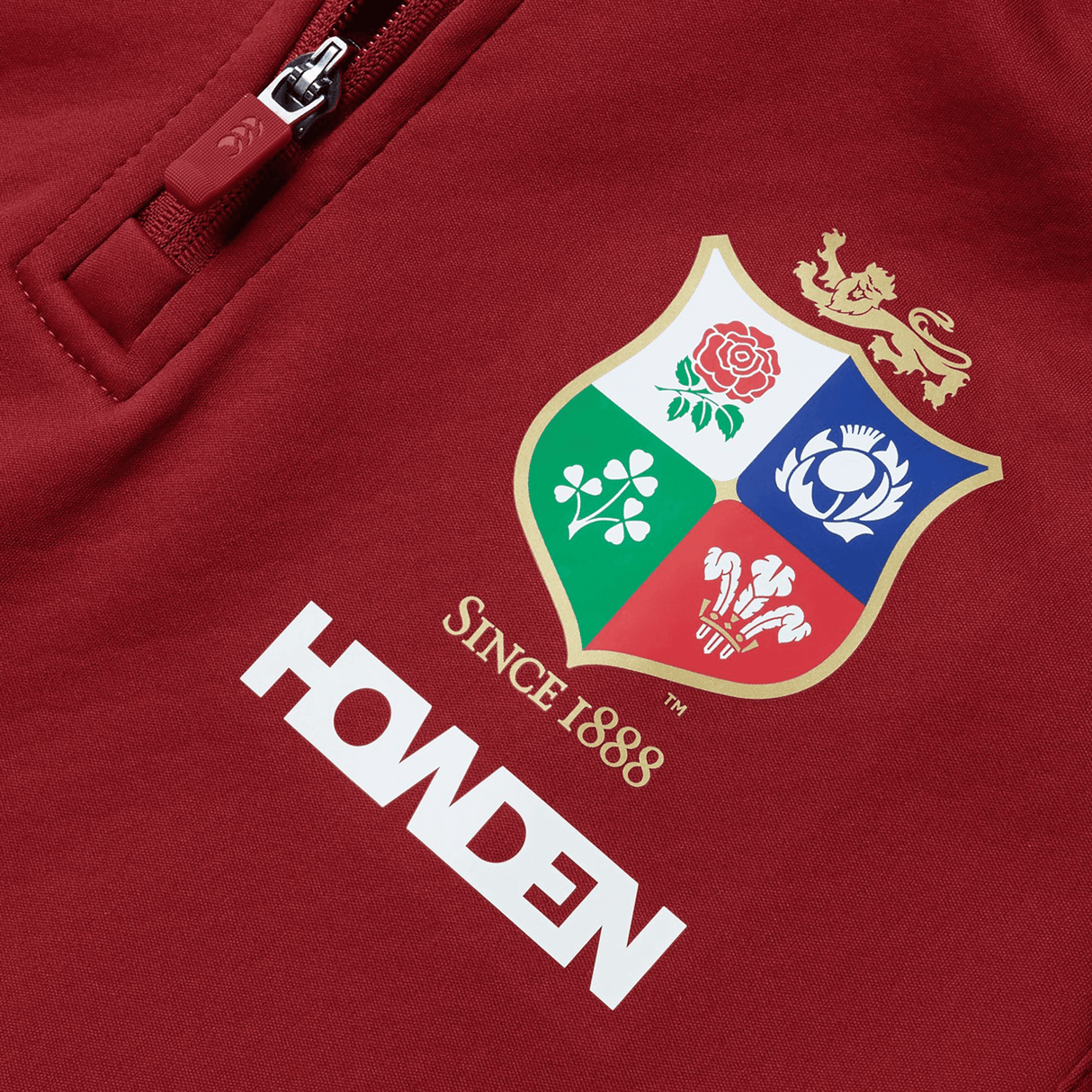 The Women's British & Irish Lions 2025 1/4 Zip Fleece by Canterbury is a stylish red top featuring a women's fit design. It proudly displays the British & Irish Lions' crest with four emblems and a majestic lion on top. The fleece is adorned with the text "Since 1888" and "HOWDEN," blending historical elements with modern style.