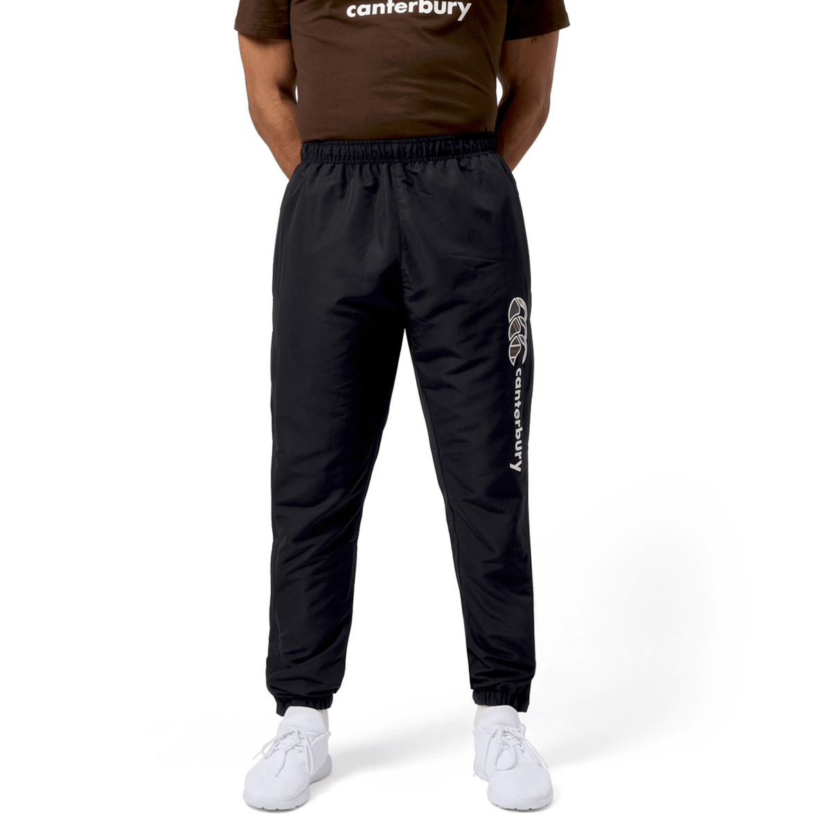 Someone is wearing black Canterbury Uglies Cuffed Stadium Pants with white sneakers against a pristine white background.