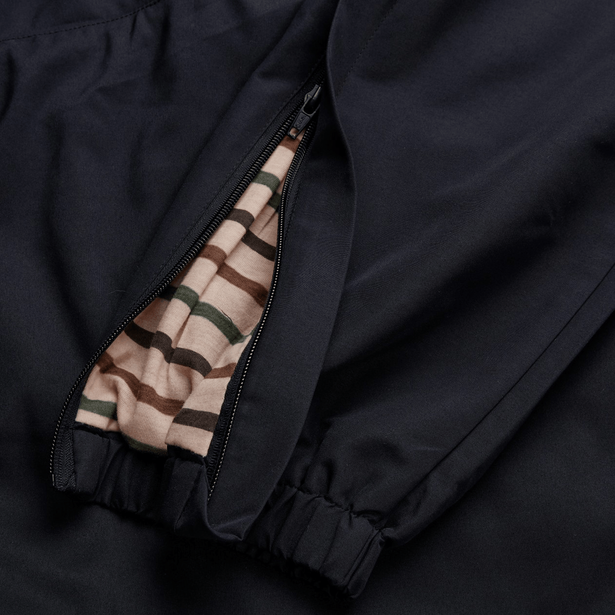 The Canterbury Uglies Cuffed Stadium Pant features a classic aesthetic with an open zipper displaying a striped fabric lining in beige, green, and brown tones. An elastic cuff completes its design.