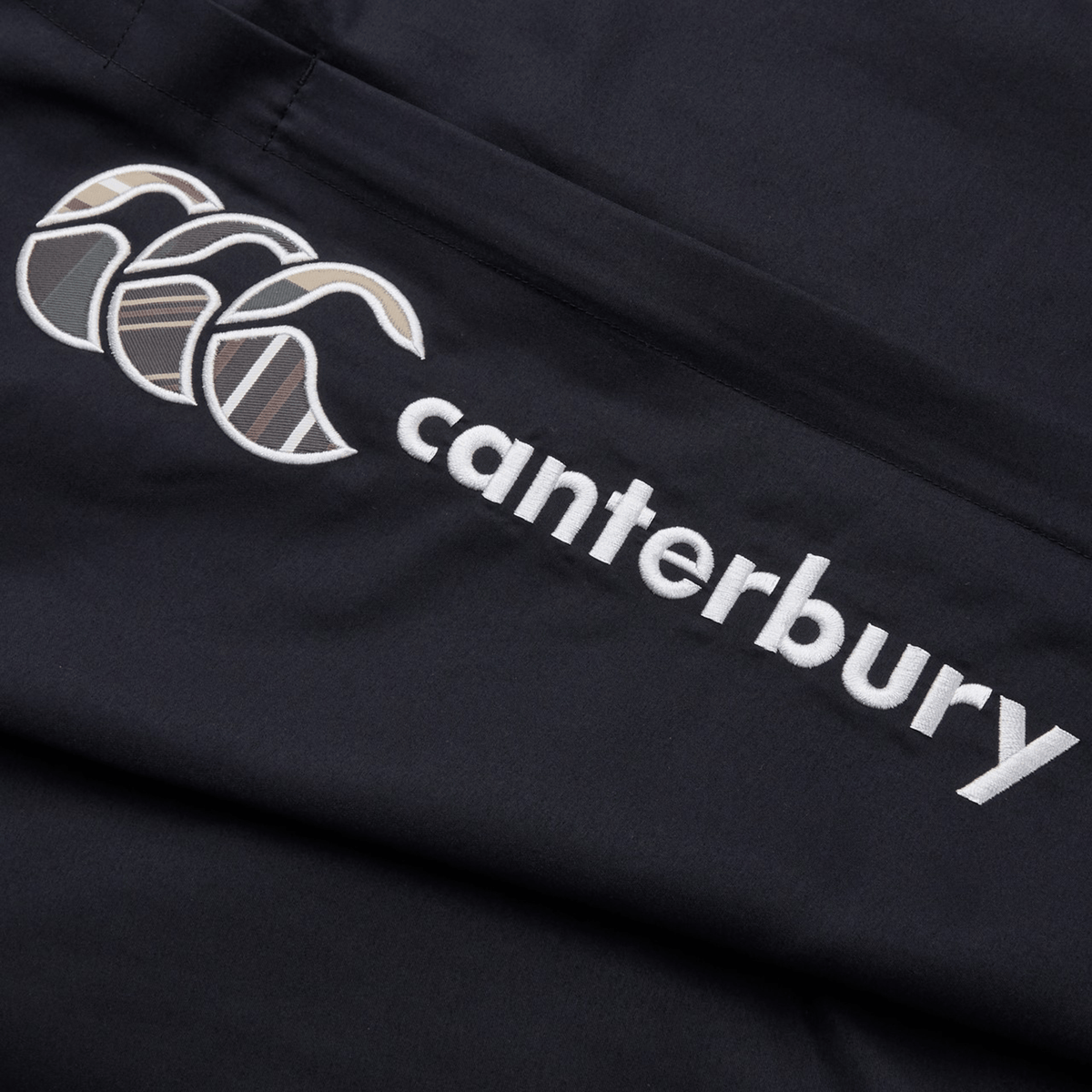 The Canterbury Uglies Cuffed Stadium Pant features a black fabric with a white embroidered Canterbury logo of three overlapping curved shapes, ideal for rugby style enthusiasts or fans appreciating classic sportswear elegance.