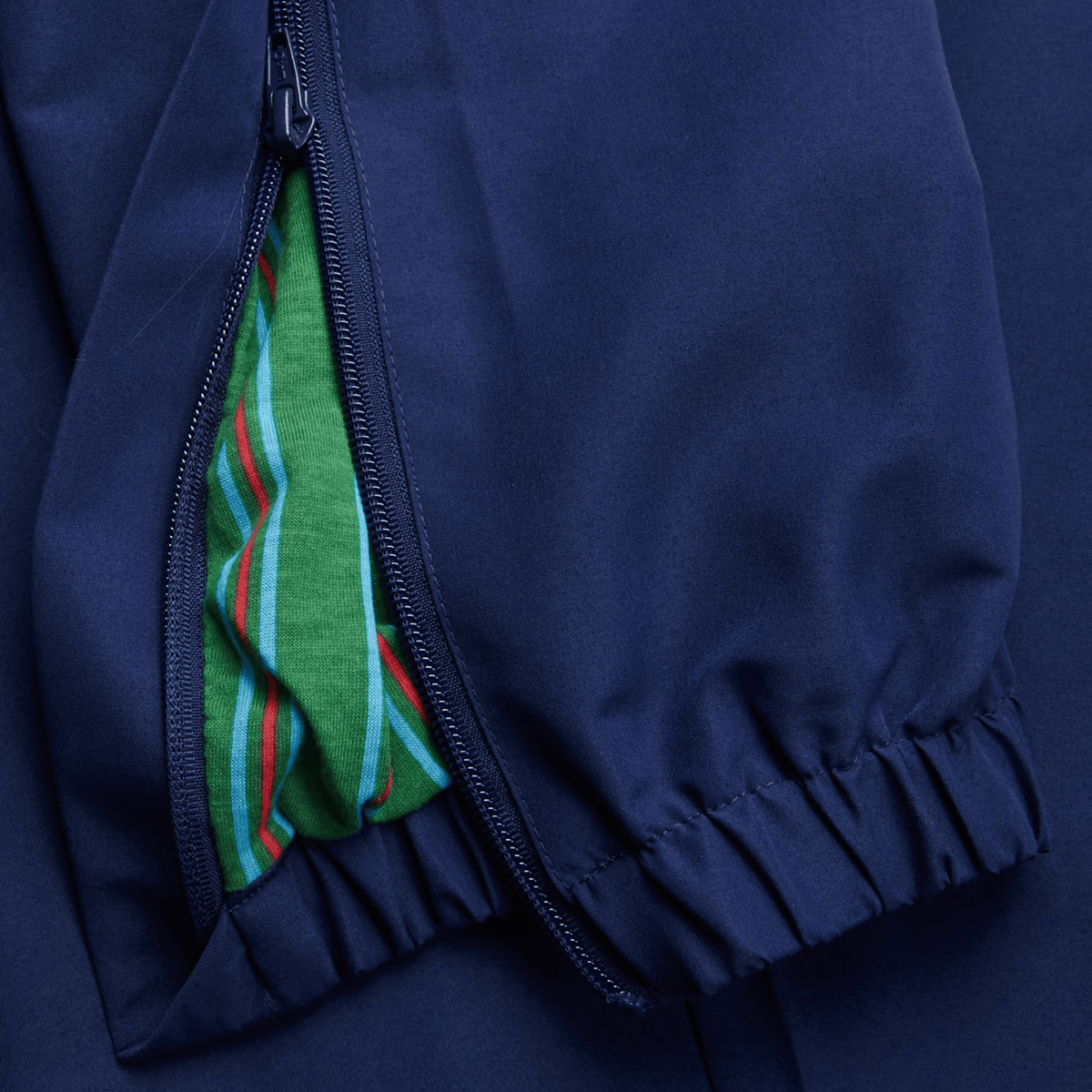 A close-up of the Canterbury Uglies Cuffed Stadium Pant reveals a navy sleeve with a green rugby-striped lining, visible through the half-open zipper.