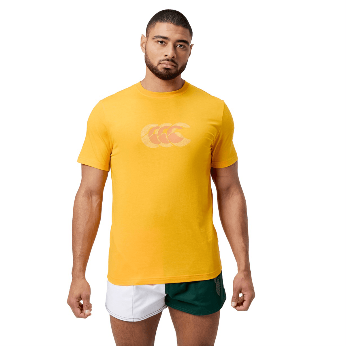A man stands against a white background, wearing a Canterbury Fundamental T-Shirt with the classic CCC logo, paired with green and white shorts.