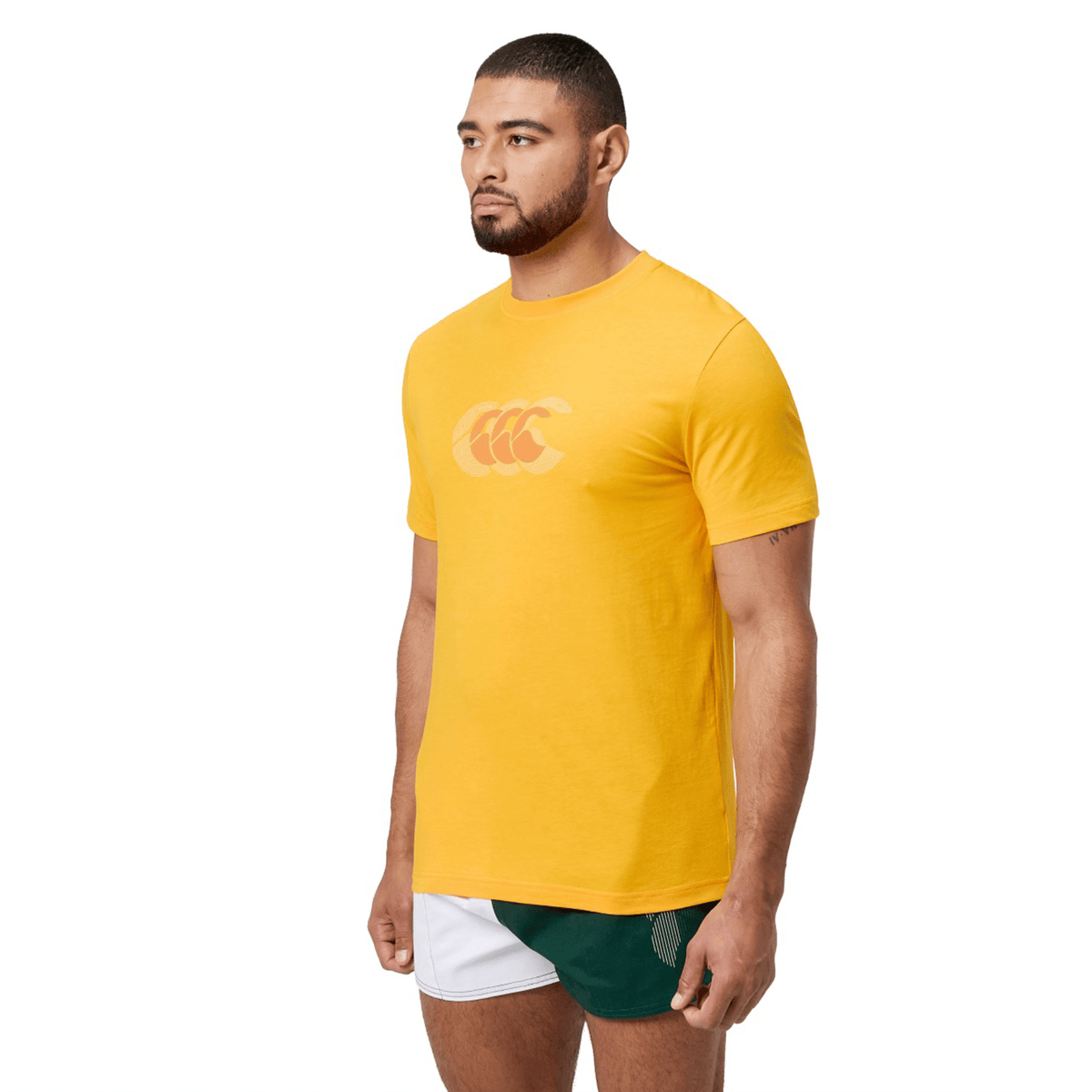 A man stands against a white background, looking to the side while wearing a classic fit Canterbury Fundamental T-Shirt paired with green shorts, showcasing the CCC logo.