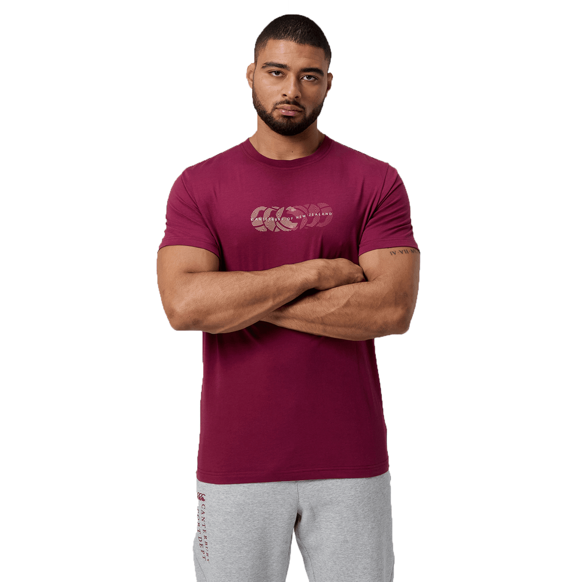 A person in a maroon Canterbury Fundamental T-Shirt with classic fit stands with crossed arms against a white background, showcasing the subtly woven CCC logo into the circular motif.