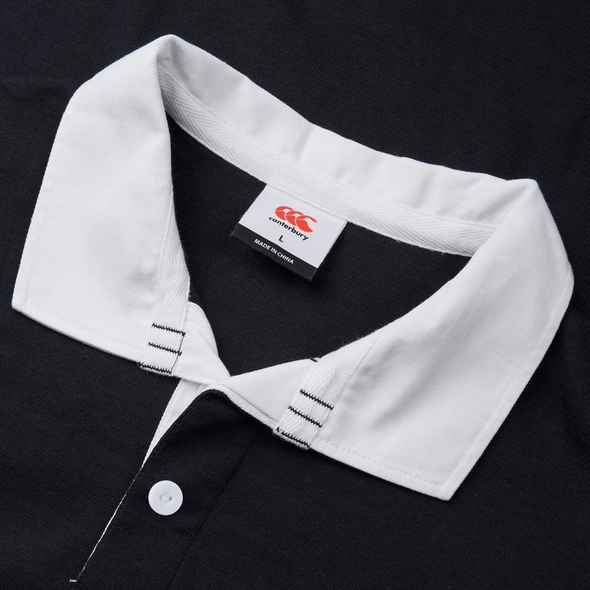 Close-up of the Canterbury Yarn Dye Short Sleeve Rugby Jersey, showcasing a black polo shirt with a white collar and buttons, crafted with precision, and featuring the iconic Canterbury label.