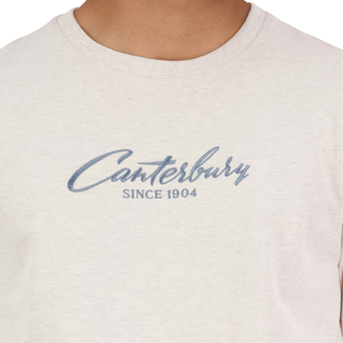 A person wearing a Canterbury Heritage Script T-Shirt, made of organic cotton and featuring the text "Canterbury Since 1904" in stylish blue cursive.