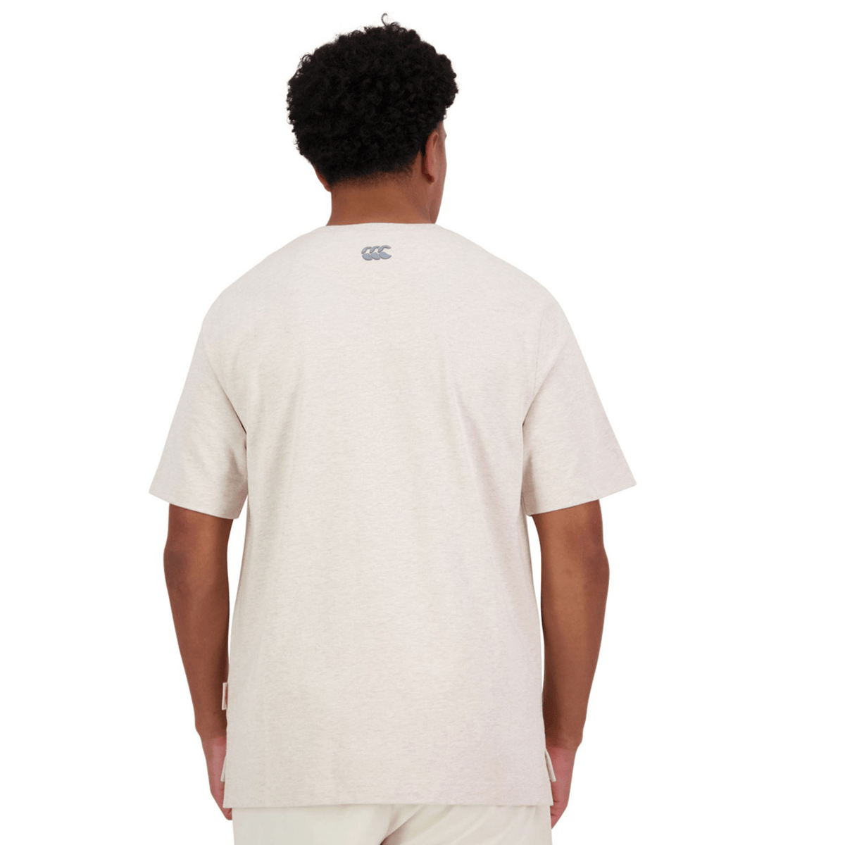A person wearing the Canterbury Heritage Script T-Shirt in beige, made from organic cotton and featuring a small logo on the back, stands with their back to the camera.
