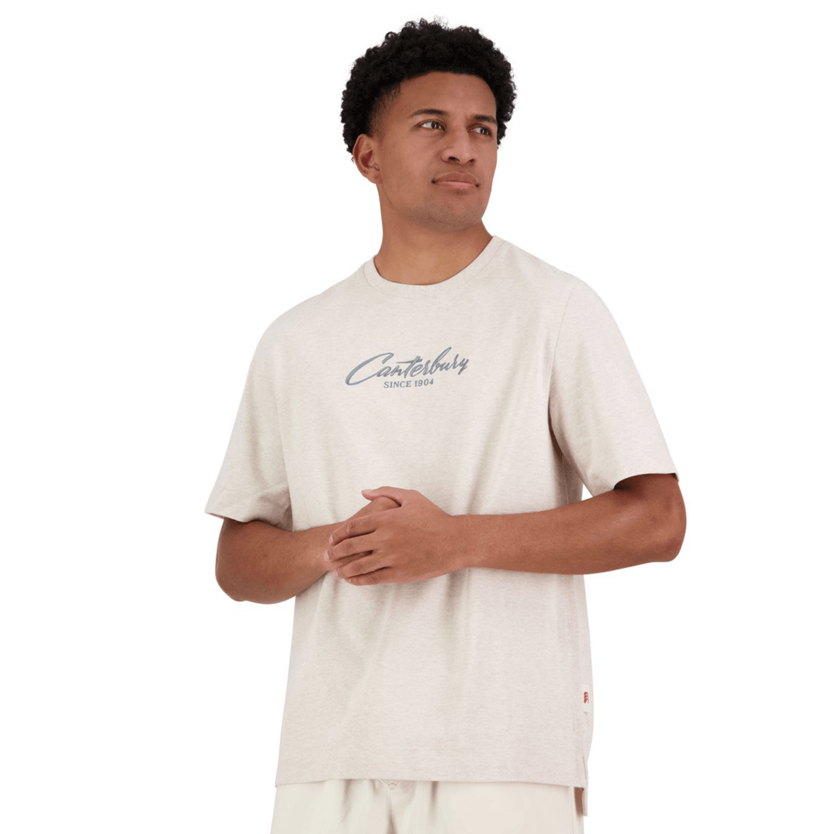 A person is wearing a Canterbury Heritage Script T-Shirt made from organic cotton in light beige, featuring "Canterbury Since 1904" on the front.