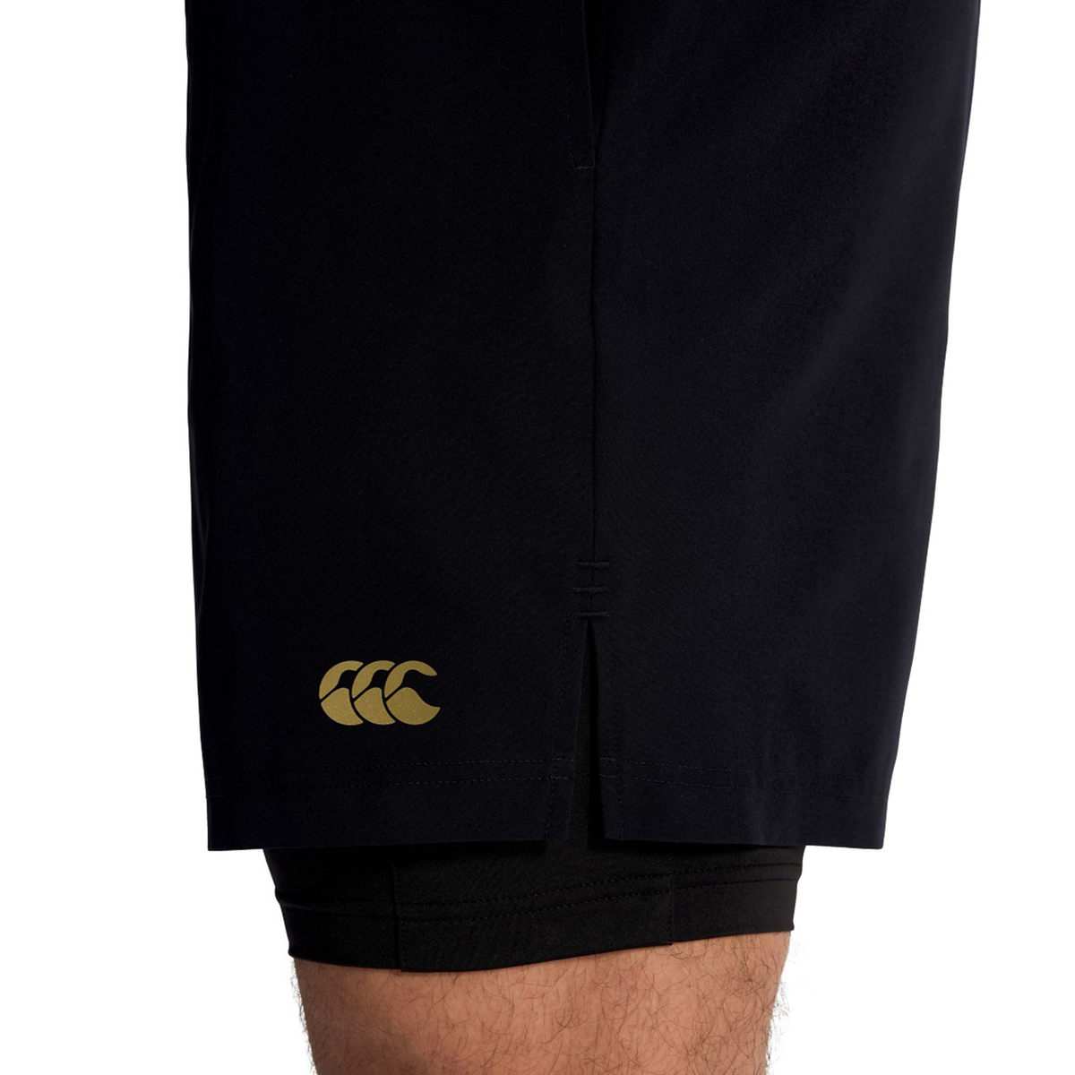 Close-up of a person's lower thigh wearing Canterbury Tempo+ 5" 2-In-1 Shorts, showing a small yellow logo on the side and a visible inner black layer.