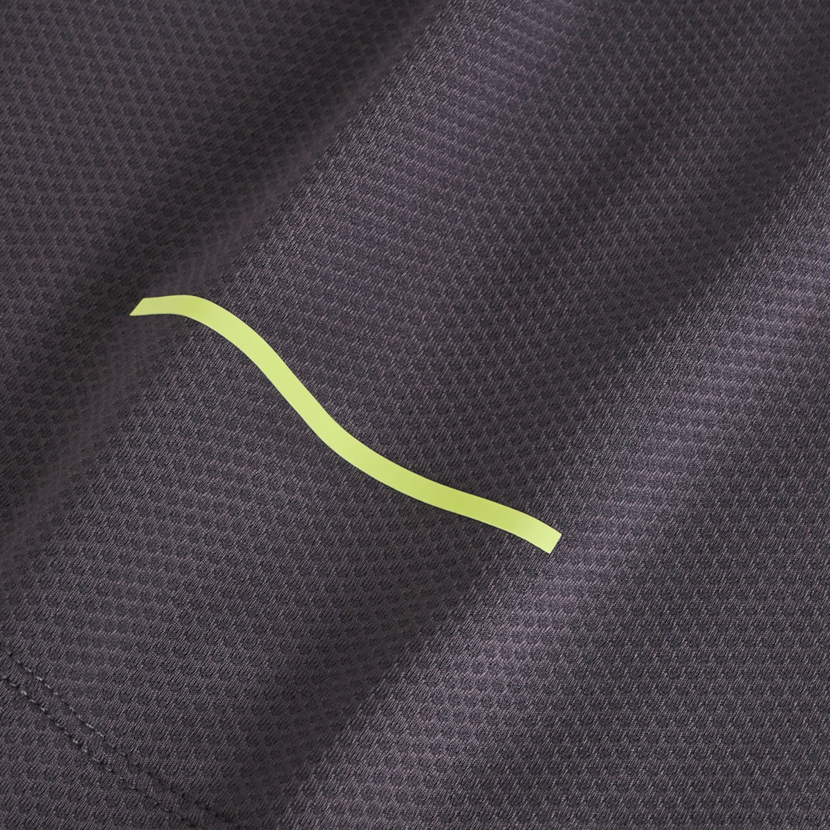 Close-up of textured dark gray fabric from the Canterbury Tempo+ Training Tank, featuring a single yellow wavy line and moisture-wicking properties.