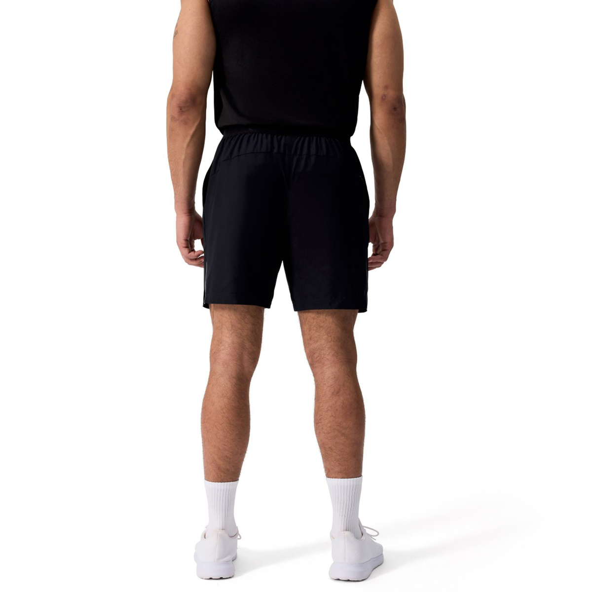 A man faces away, wearing a black sleeveless shirt and Canterbury Tempo+ 7" Training Shorts, paired with white socks and sneakers, against a plain white background.