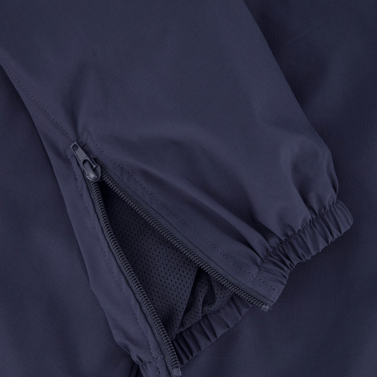 Close-up of the Canterbury Tempo+ Training Trackpant in navy, showcasing a bi-stretch fabric sleeve with an elastic cuff and partially open zipper revealing a mesh lining.