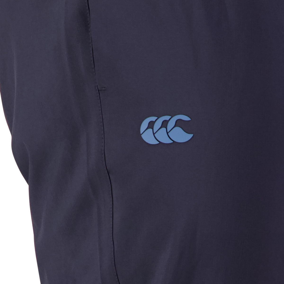 Close-up of a Canterbury Tempo+ Training Trackpant in navy blue, made from bi-stretch fabric, featuring a small blue logo with three stylized waves on its tapered fit design.