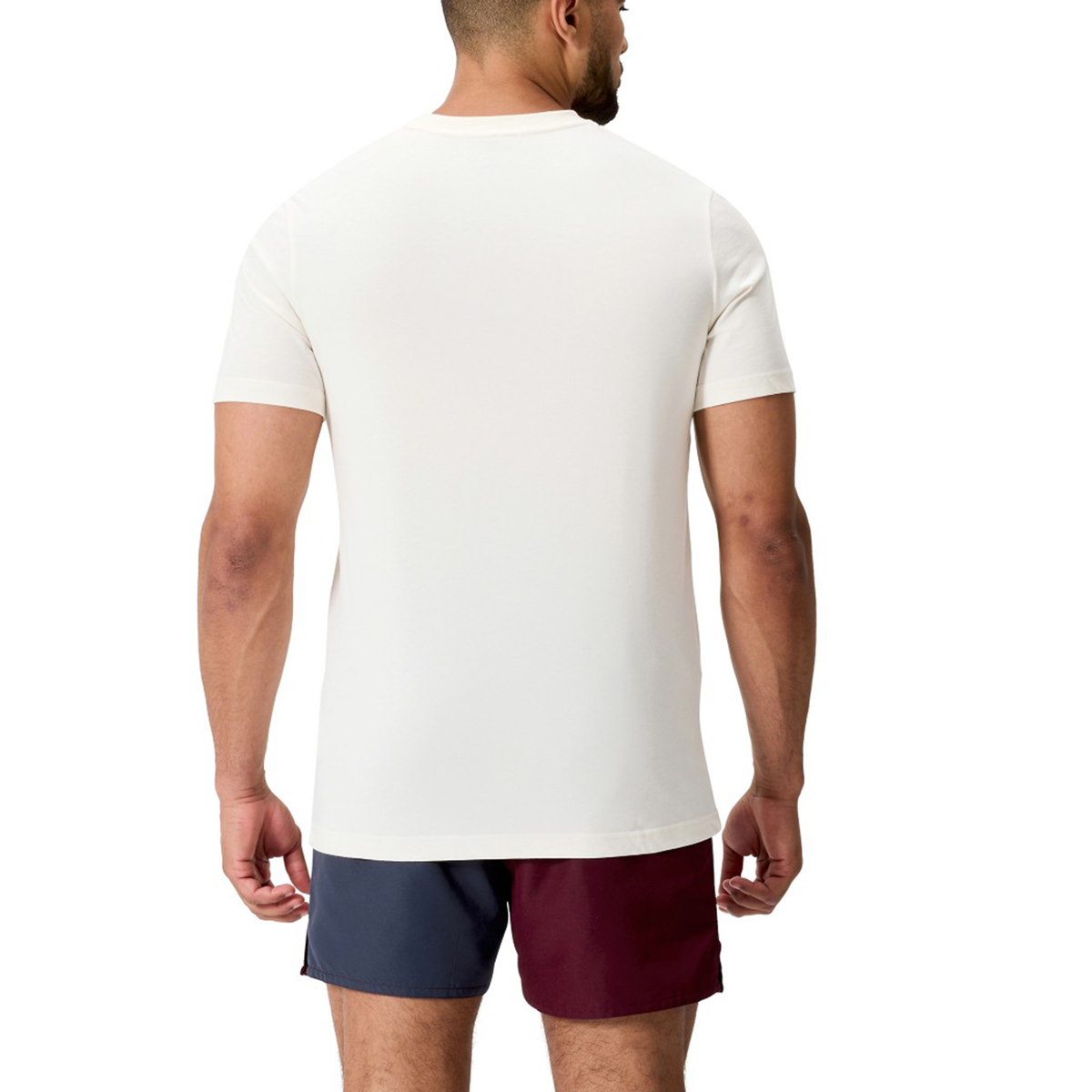 A man stands with his back to the camera, wearing a Fundamentals CCC Logo T-Shirt by Canterbury and two-tone shorts—one leg blue, one maroon—for a clean, fundamentals-inspired look.
