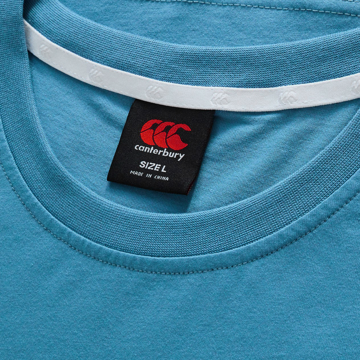 Close-up of the Canterbury Fundamentals CCC Logo T-Shirt in blue, featuring a visible black size L tag and "Made in China" under the collar—a genuine piece from Canterbury's core collection.